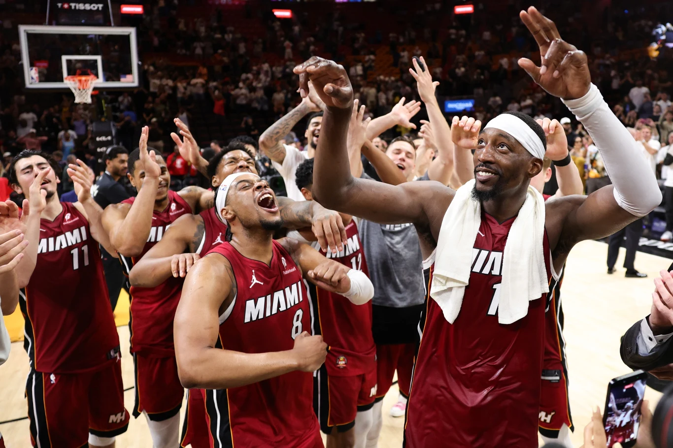 Koszykarze drużyny Miami Heat w czerwonych strojach świętują zwycięstwo na parkiecie, unosząc ręce w górę, uśmiechając się i okazując radość po meczu.