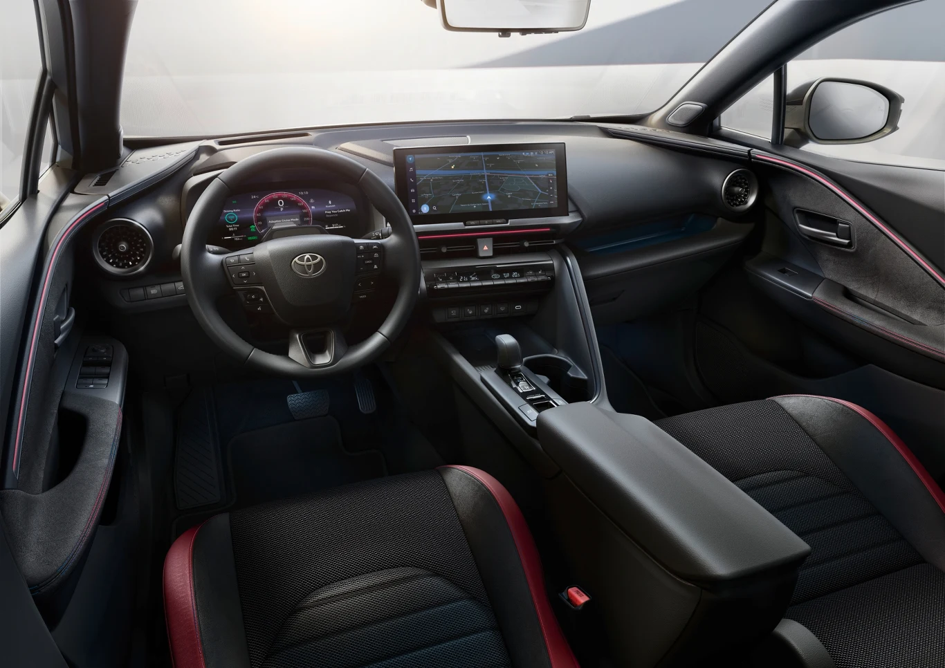 Wnętrze nowoczesnego samochodu z cyfrowym zestawem wskaźników za kierownicą, dużym centralnym ekranem multimedialnym, czarną deską rozdzielczą z czerwonymi akcentami oraz wygodnymi siedzeniami z tapicerką materiałową.