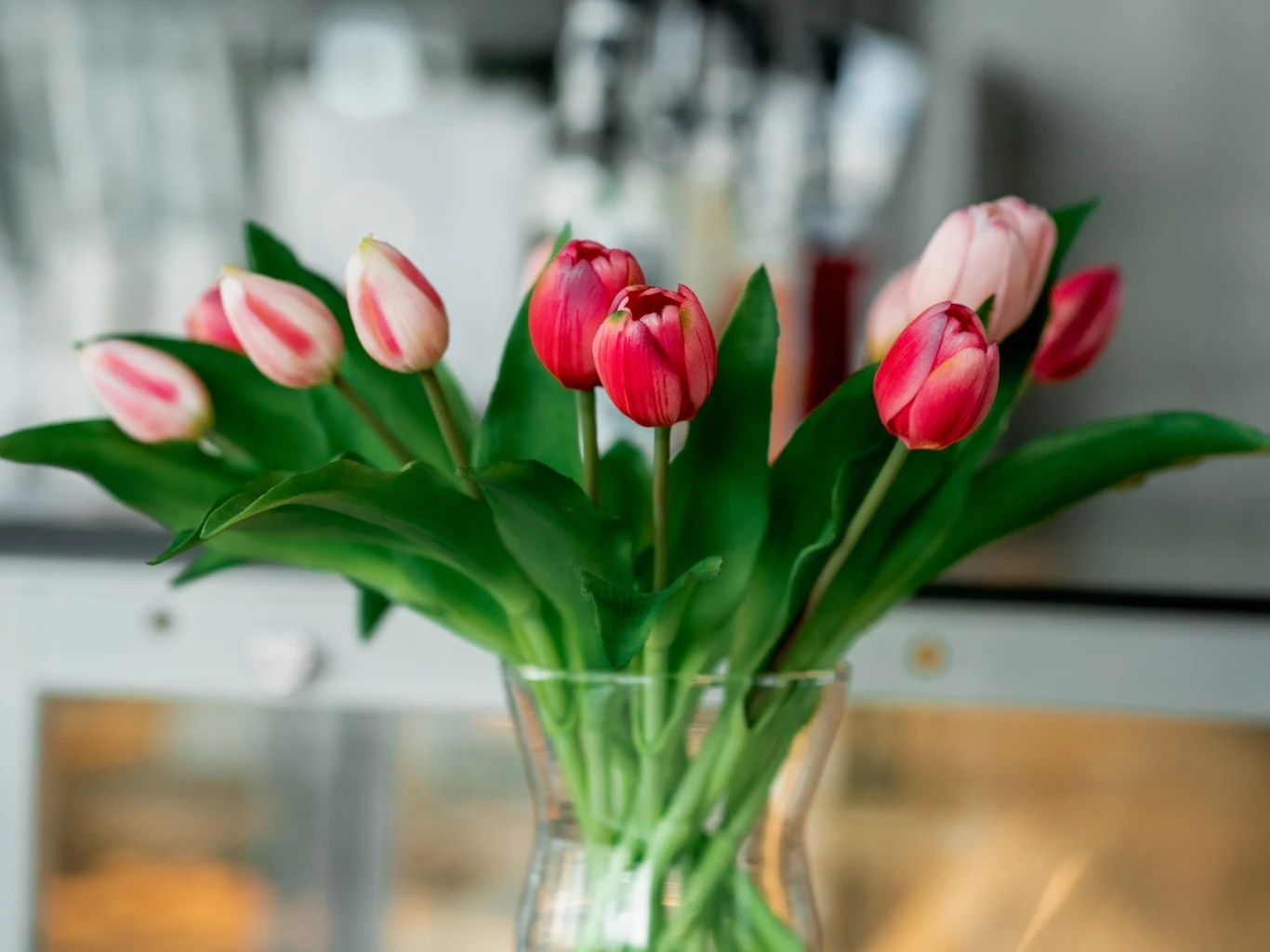 Bukiet różowych tulipanów z zielonymi liśćmi umieszczony w przezroczystym szklanym wazonie. 