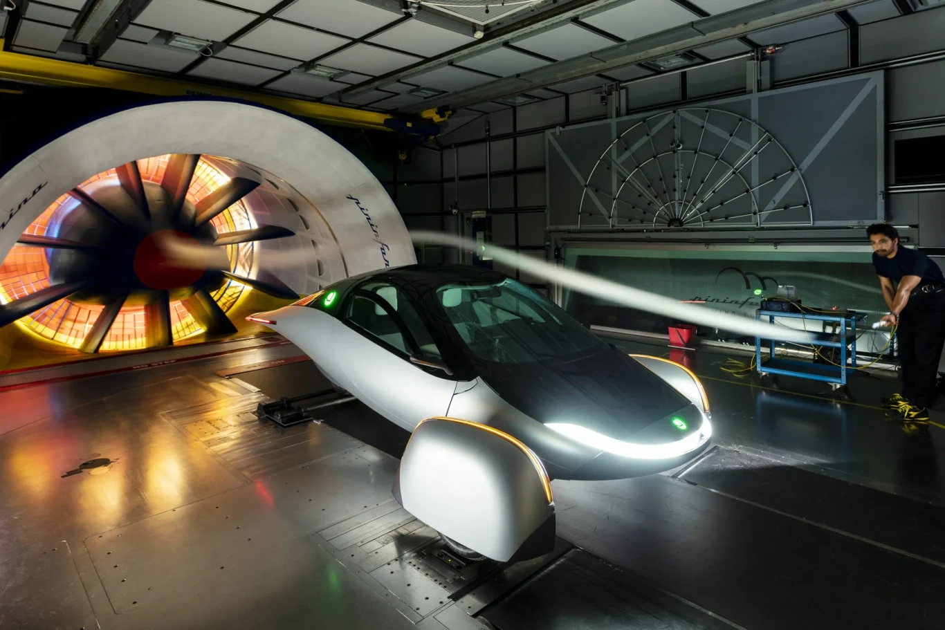 Nowoczesny samochód elektryczny o futurystycznym kształcie testowany w tunelu aerodynamicznym, z widocznym strumieniem powietrza przepływającym przez karoserię i technikiem nadzorującym pomiary.