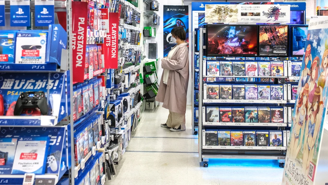 Kobieta przeglądająca półki z grami na konsole PlayStation i Xbox w sklepie z elektroniką.