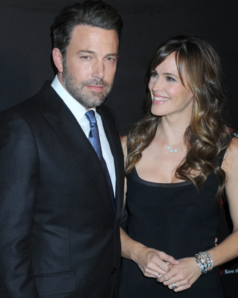 Elegancko ubrany mężczyzna w garniturze i kobieta w czarnej sukni stoją obok siebie, kobieta uśmiecha się serdecznie, trzymając mężczyznę za ramię.