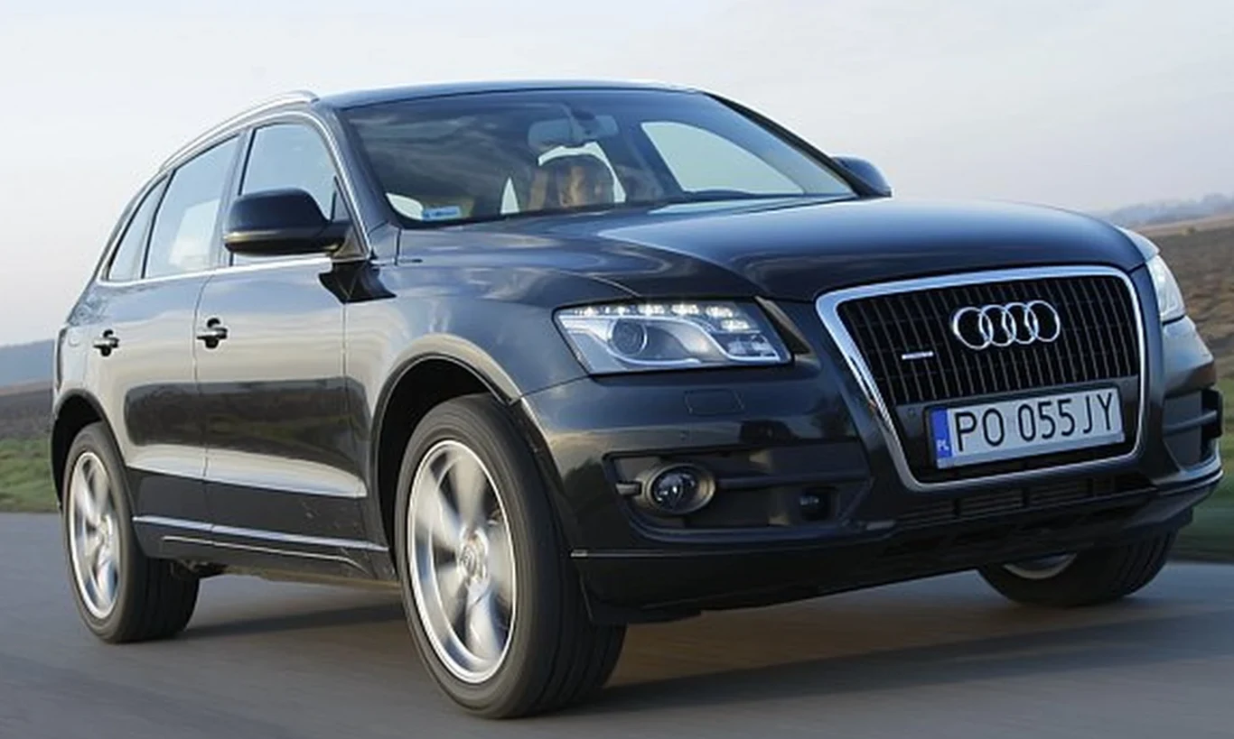 Czarny SUV marki Audi z polską rejestracją, jadący po asfaltowej drodze, widoczny z przodu i z boku, dynamicznie uchwycony w ruchu.