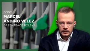 Mężczyzna w okularach i garniturze siedzi na tle zielonej grafiki z wizerunkiem dystrybutorów paliw oraz napisem informującym o gościu programu, Marcelu Andino Velez z Greenpeace Polska.