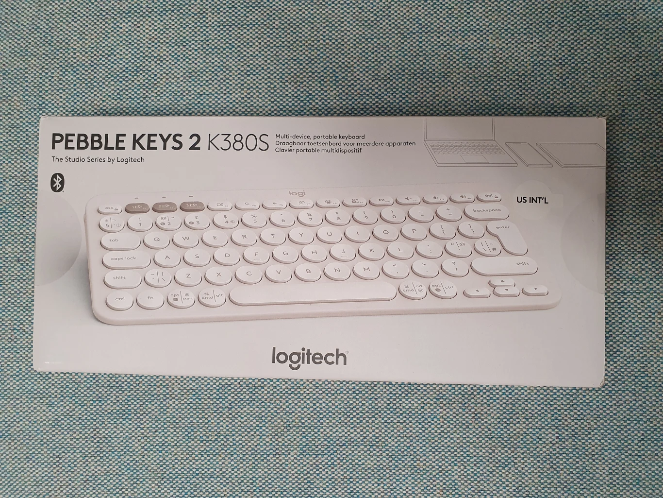 Białe, kompaktowe klawiatura bezprzewodowa Logitech Pebble Keys 2 K380S na tle pudełka z logotypem marki oraz nazwą modelu, wyróżniające się okrągłymi klawiszami i minimalistycznym designem.