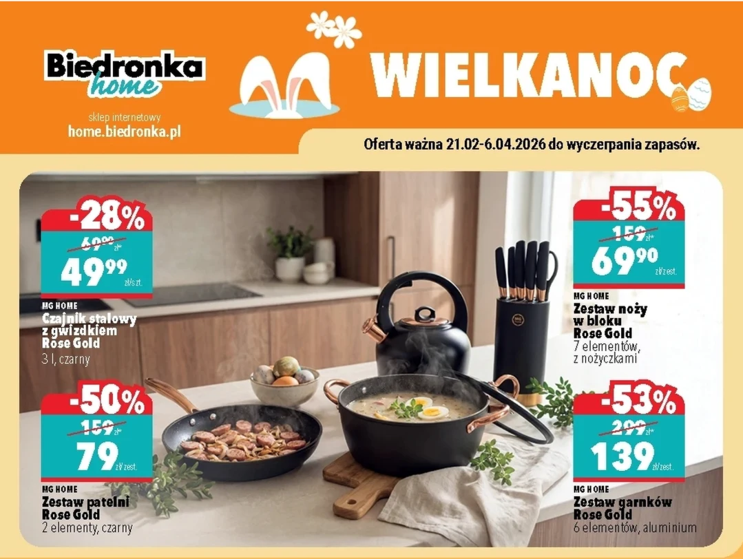 Zestaw nowoczesnych, czarnych naczyń kuchennych z serii Rose Gold na blacie kuchennym, w tym patelnia, rondel z uchwytem oraz komplet noży w eleganckim stojaku; na pierwszym planie dania przygotowane w naczyniach, a tło stanowi jasna, minimalistyczna k...