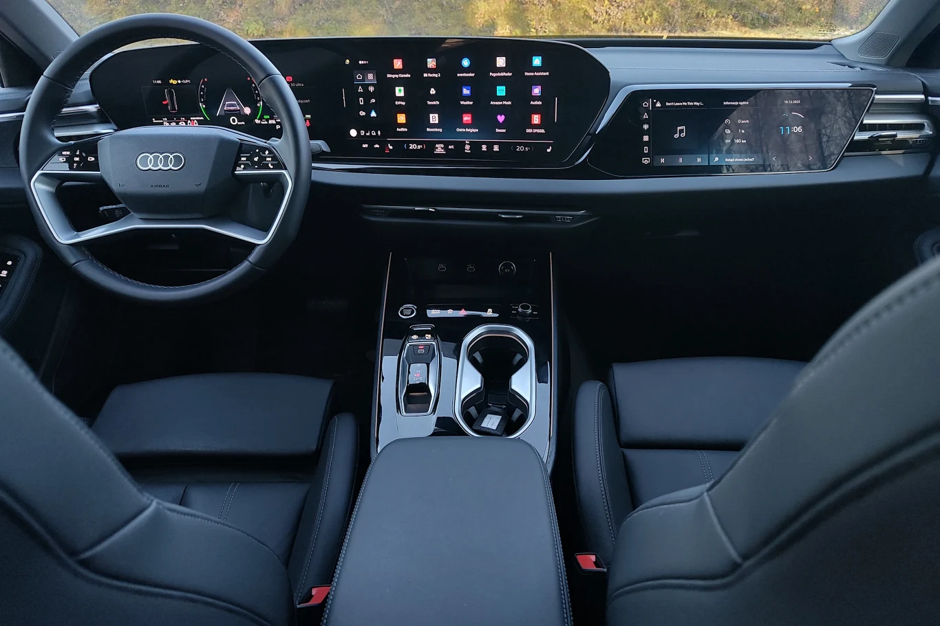 Wnętrze nowoczesnego samochodu Audi z cyfrowym kokpitem, dużym panoramicznym ekranem dotykowym, panelem sterowania na konsoli środkowej oraz dwoma czarnymi, komfortowymi fotelami.