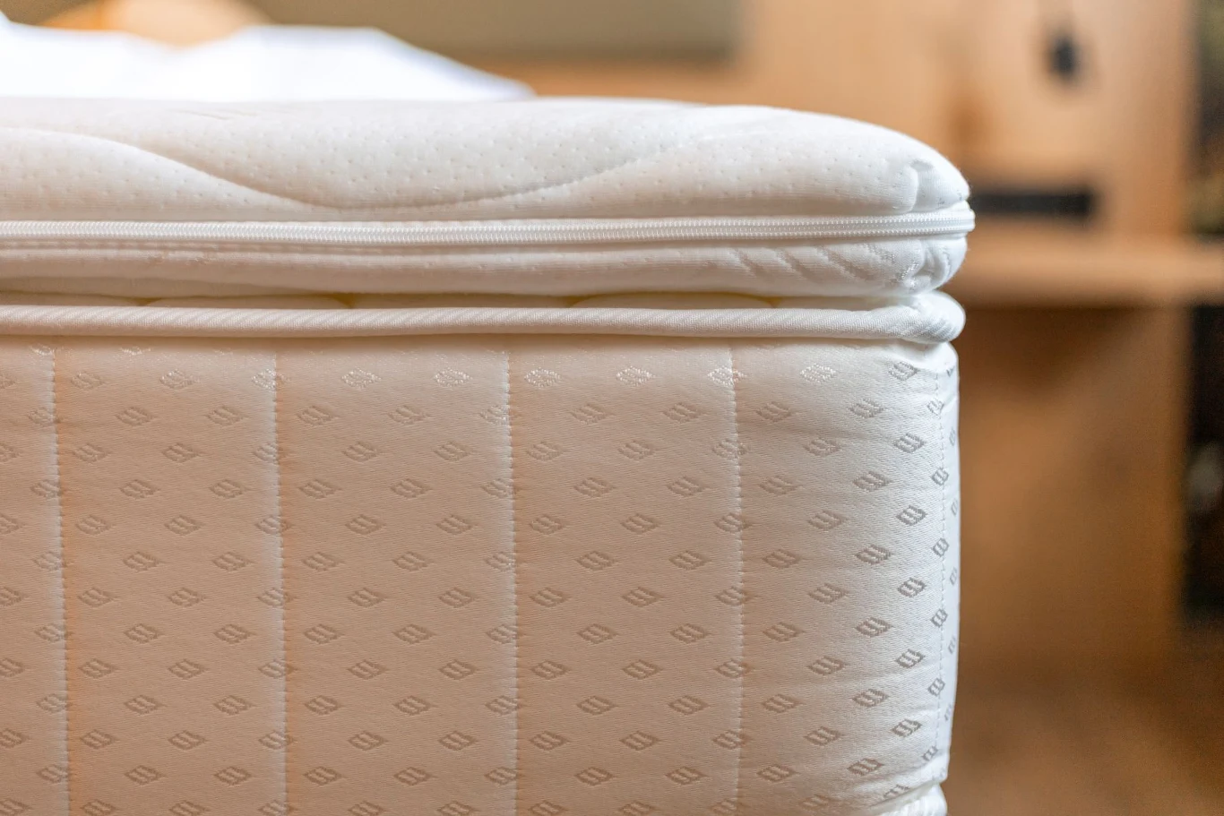 Gruba, jasna warstwa materaca z delikatnym wzorem i zamkiem błyskawicznym, wyraźnie ukazująca miękką, pikowaną powierzchnię górną.
