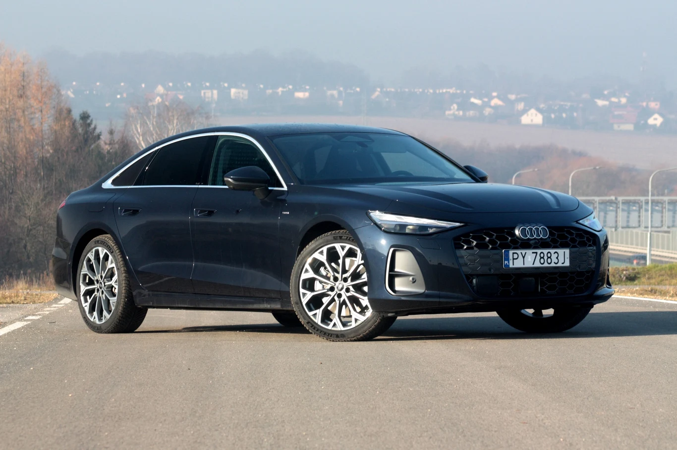 Czarny samochód marki Audi o sportowej sylwetce stoi na pustej drodze, wyróżnia się dużymi felgami i charakterystycznym przodem z podwójnymi reflektorami LED.