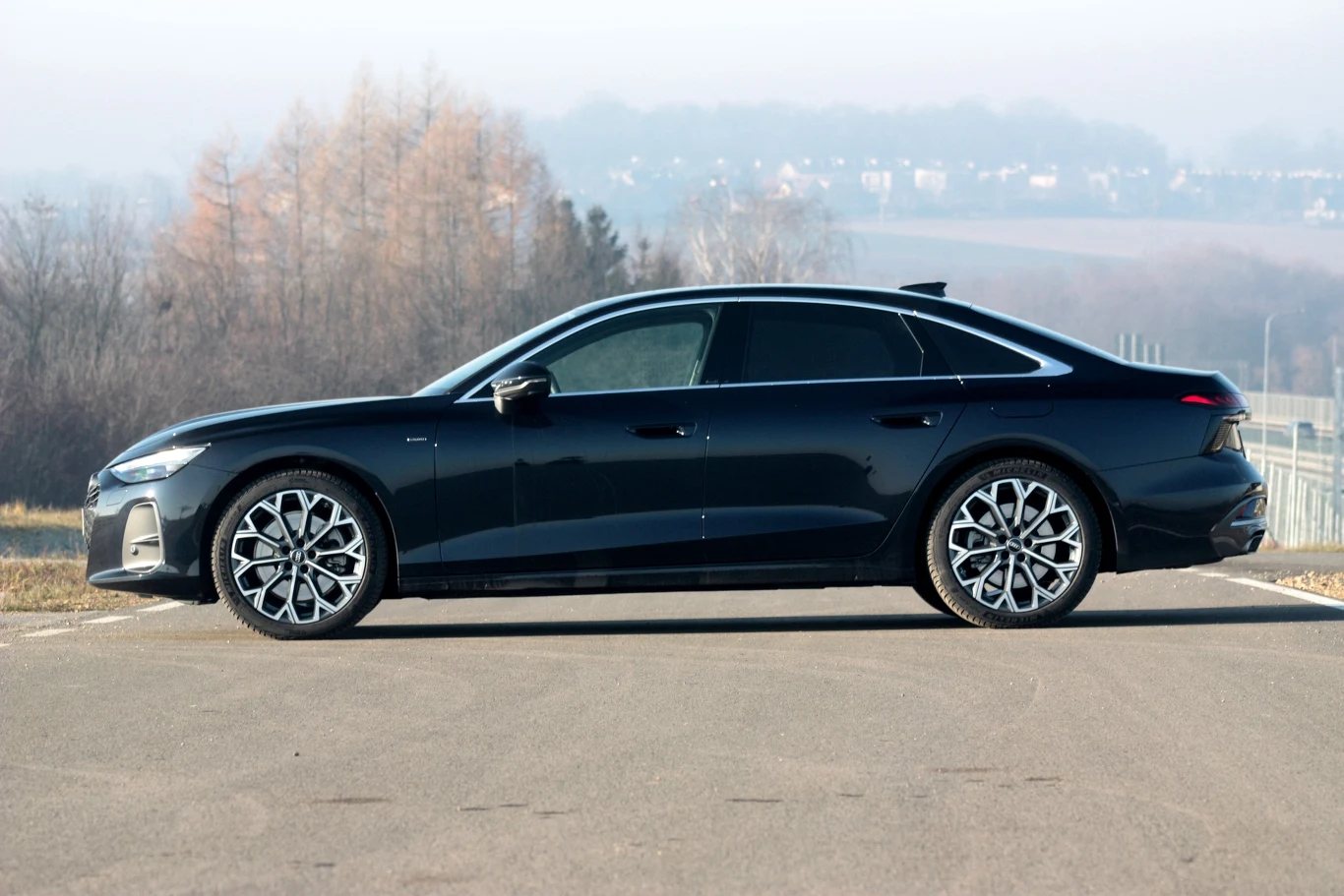 Luksusowy czarny samochód elektryczny o aerodynamicznym nadwoziu, dużych aluminiowych felgach i przyciemnianych szybach, ustawiony na asfalcie w otoczeniu delikatnie zamglonego krajobrazu.