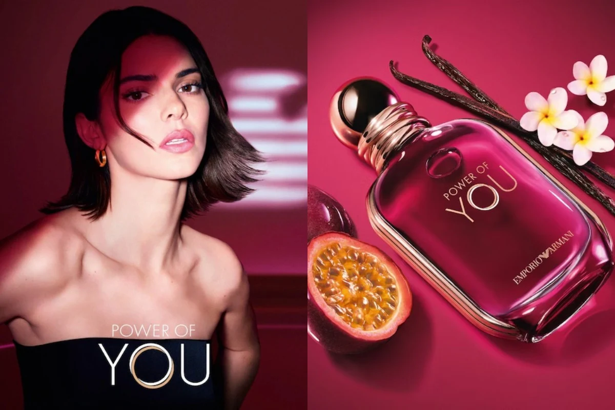 Elegancka kobieta z krótkimi, ciemnymi włosami i złotymi kolczykami, w tle flakon perfum Power of You marki Emporio Armani na różowym tle obok świeżej marakui oraz lasek wanilii, otoczony delikatnymi białymi kwiatami.