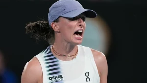 Tenisistka w sportowej koszulce i czapce z daszkiem wyraża silne emocje, szeroko otwierając usta i zaciskając szczękę podczas meczu.