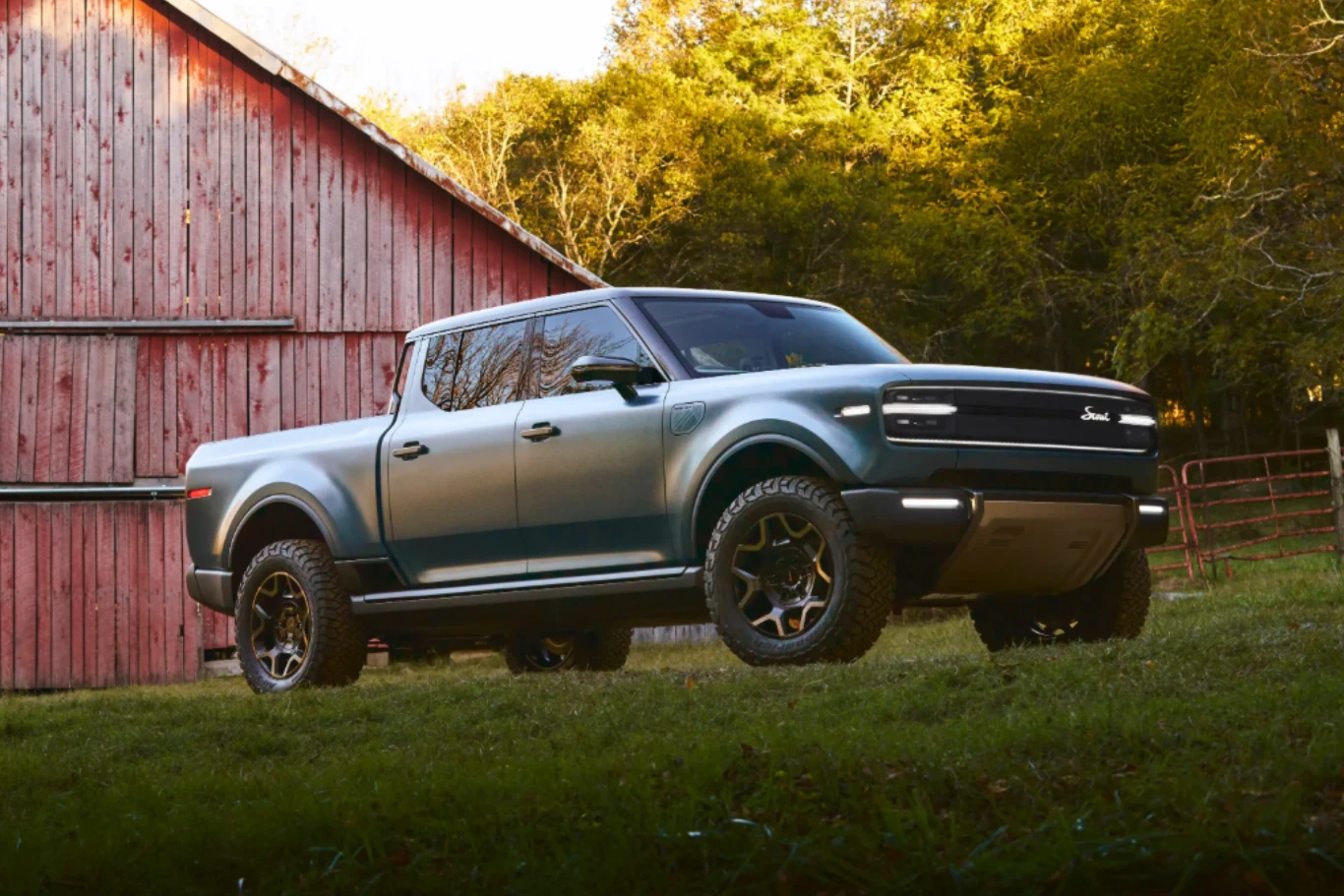 Nowoczesny zielony pickup z terenowymi oponami zaparkowany na trawie obok czerwonej drewnianej stodoły, w tle drzewa oświetlone ciepłym światłem zachodzącego słońca.