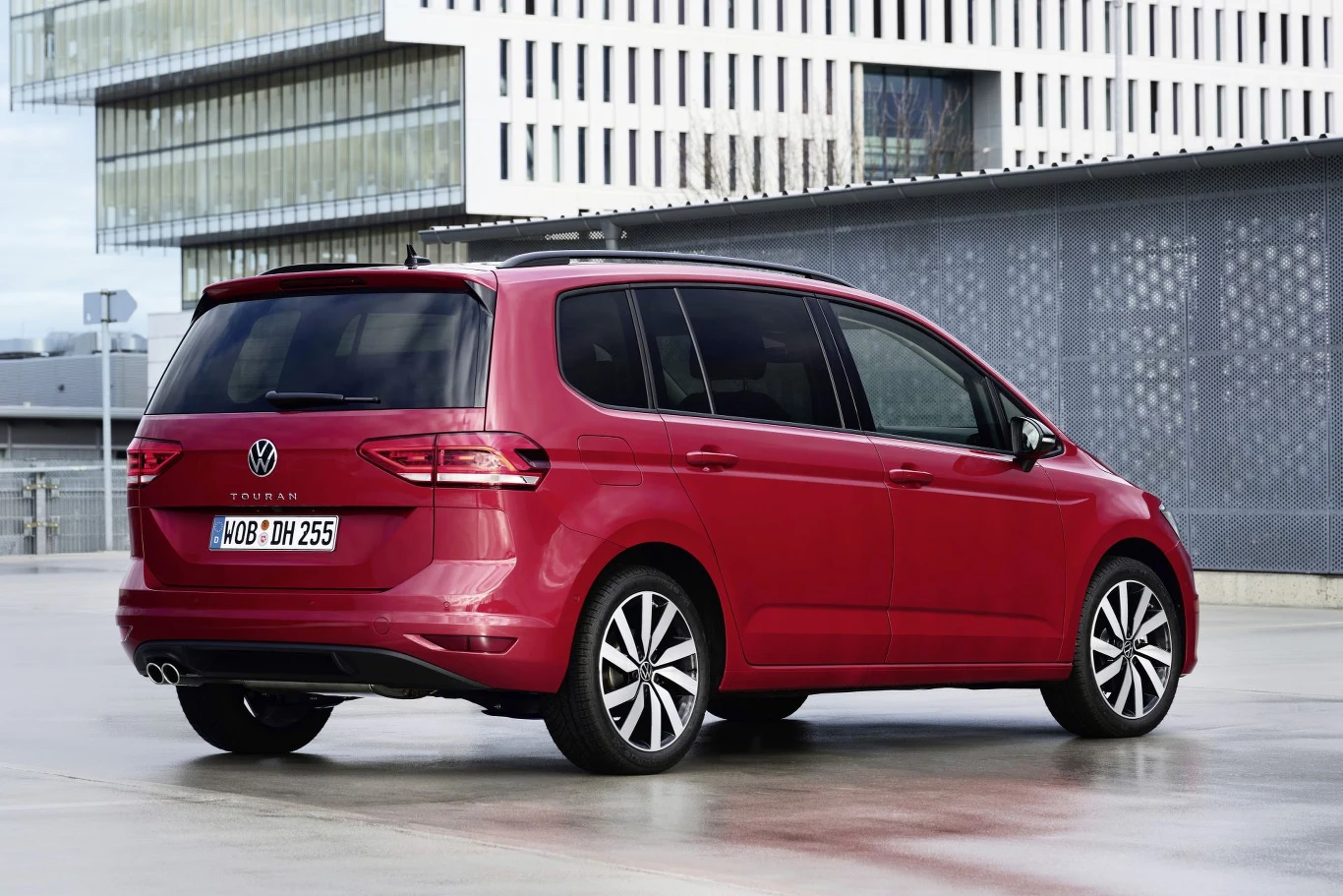 Czerwony minivan Volkswagen Touran w nowoczesnym, miejskim otoczeniu, widok z tyłu pod kątem, wyraźne reflektory LED oraz przyciemniane tylne szyby, rejestracja niemiecka.