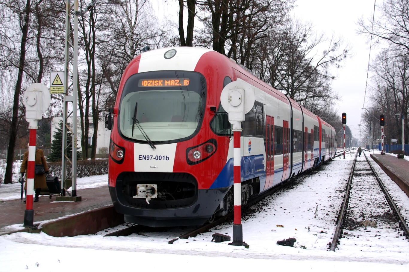 Na polskie tory wyjedzie pociąg autonomiczny. Czy to przyszłość kolei? Pociąg EN97 w barwach czerwono-niebiesko-białych na ośnieżonej stacji, widoczne perony, sygnalizatory, drzewa bez liści.
