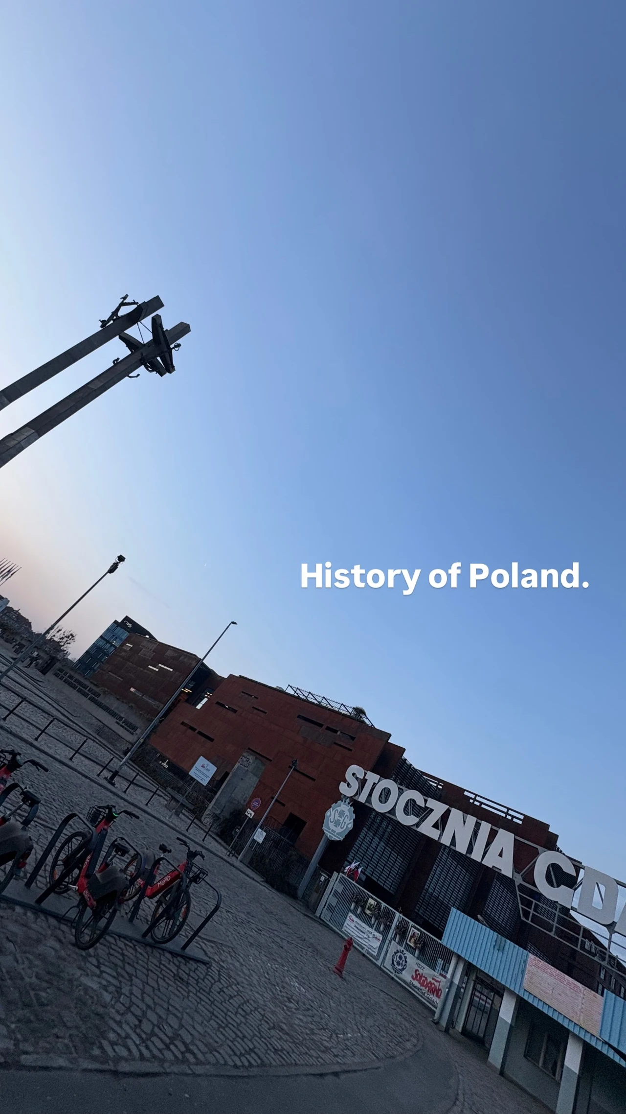 Monumentalne żurawie stoczniowe na tle industrialnych budynków Stoczni Gdańskiej, podkreślających znaczenie tego miejsca w historii Polski.