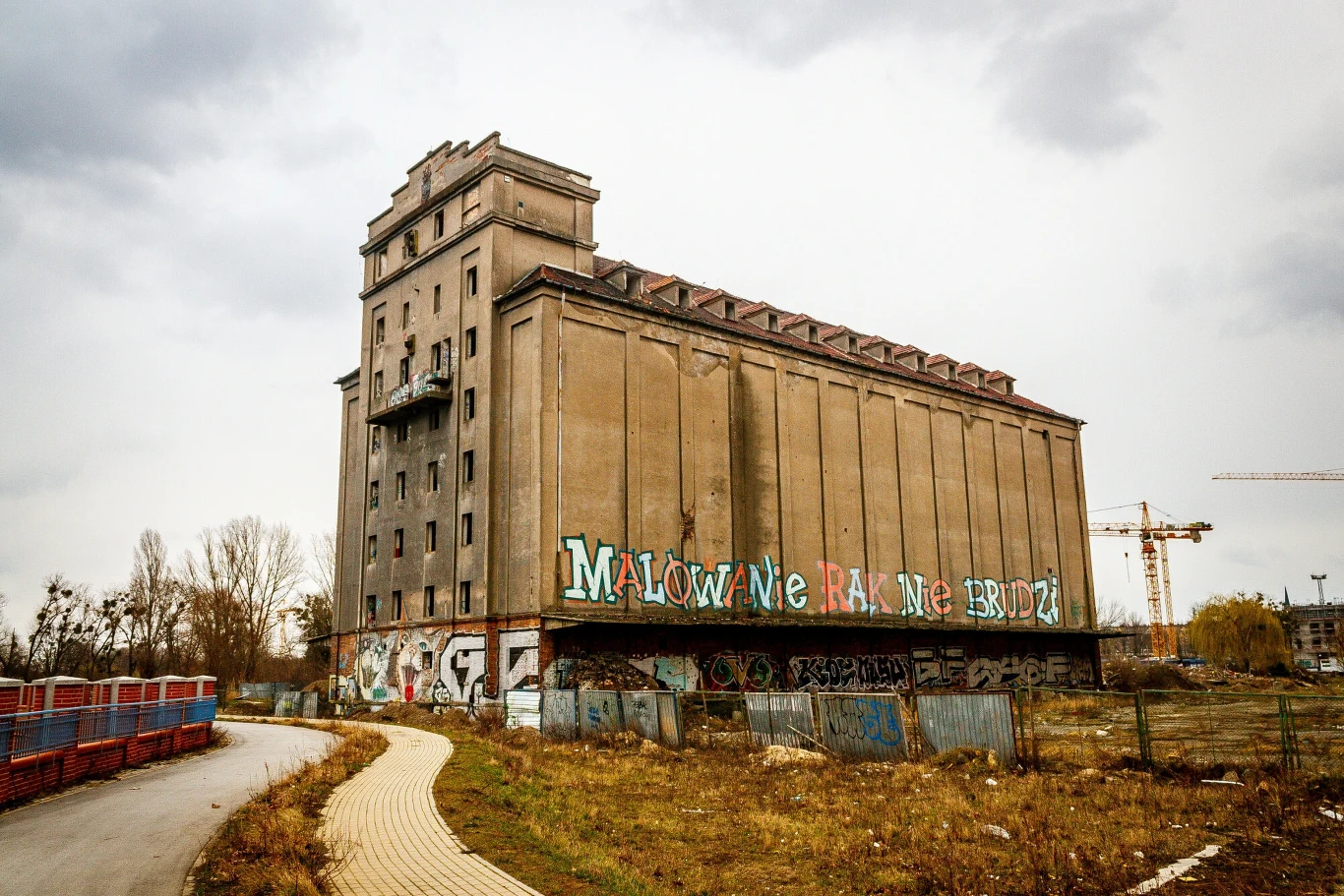 Straszył przez lata. Teraz zamieni się w luksusowe lofty Opuszczony elewator zbożowy Odra we Wrocławiu, z graffiti i napisem, otoczony ogrodzeniem i żurawiami budowlanymi.