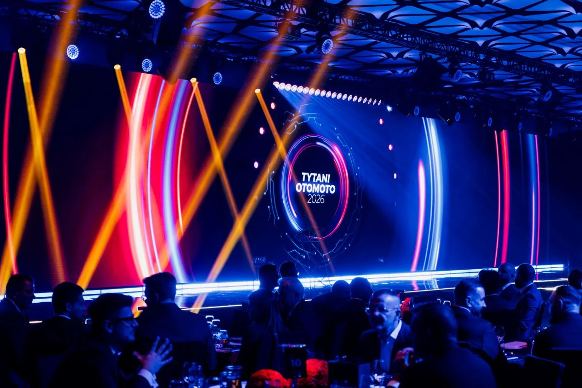 Uroczysta gala z tłumem gości siedzących przy stołach, dynamiczne kolorowe oświetlenie sceny oraz widoczne na ekranie duże logo wydarzenia 'Tytani Otomoto 2023'.