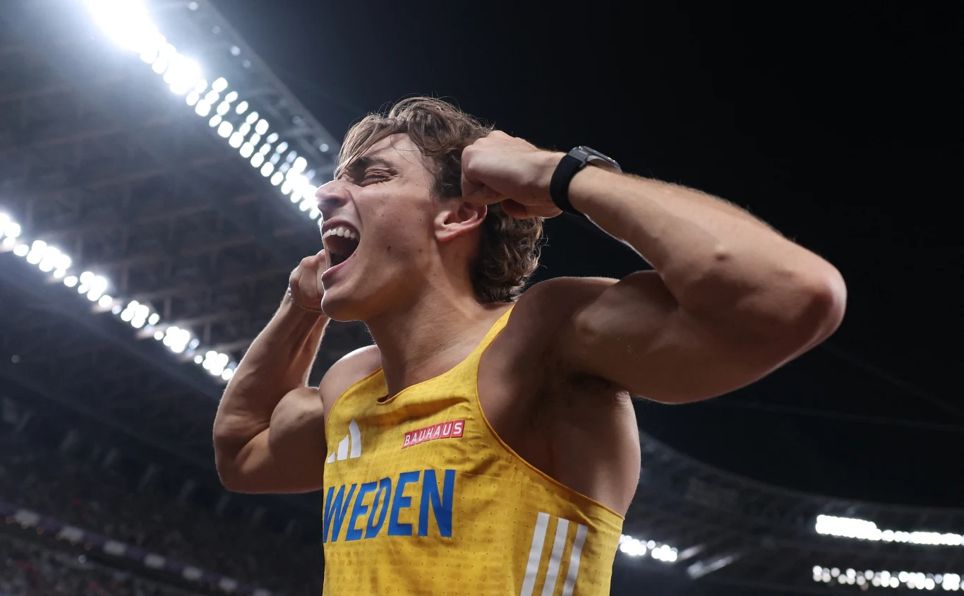 Armand Duplantis Sportowiec w żółtym stroju z napisem „Sweden”, stojący na stadionie, wyraża intensywne emocje, zaciśniętymi pięściami przy twarzy i szeroko otwartymi ustami, gestykulując triumfalnie pod światłami stadionu.
