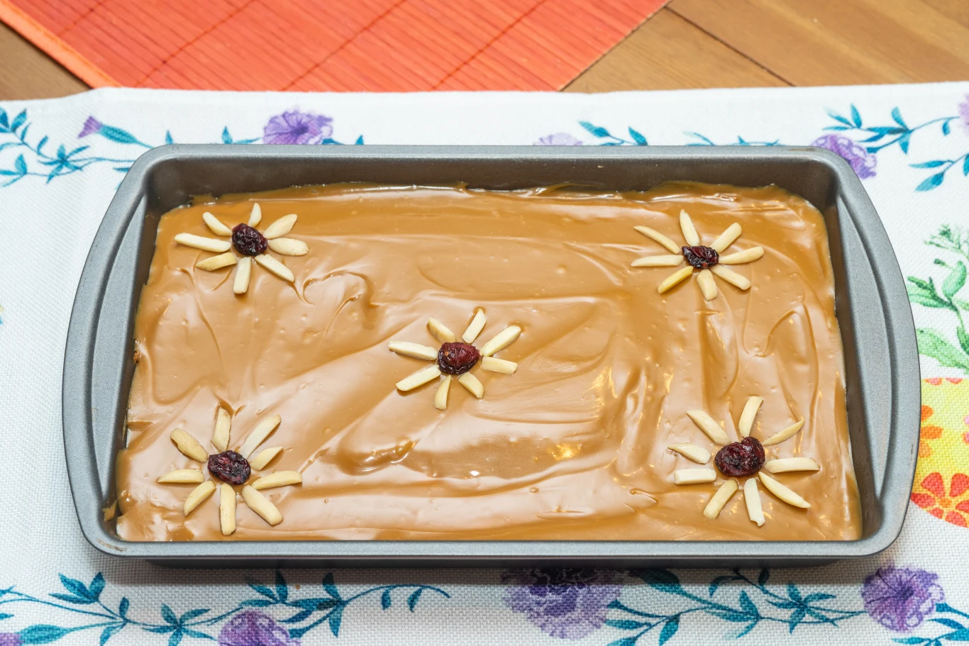Blacha z ciastem pokrytym kremem karmelowym, udekorowanym czterema kwiatami ułożonymi z migdałów i żurawin na wierzchu.