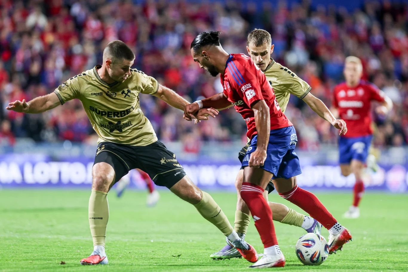 Ivi Lopez z Rakowa prowadzi piłkę na murawie podczas meczu z Górnikiem Zabrze; obok dwaj piłkarze rywali.