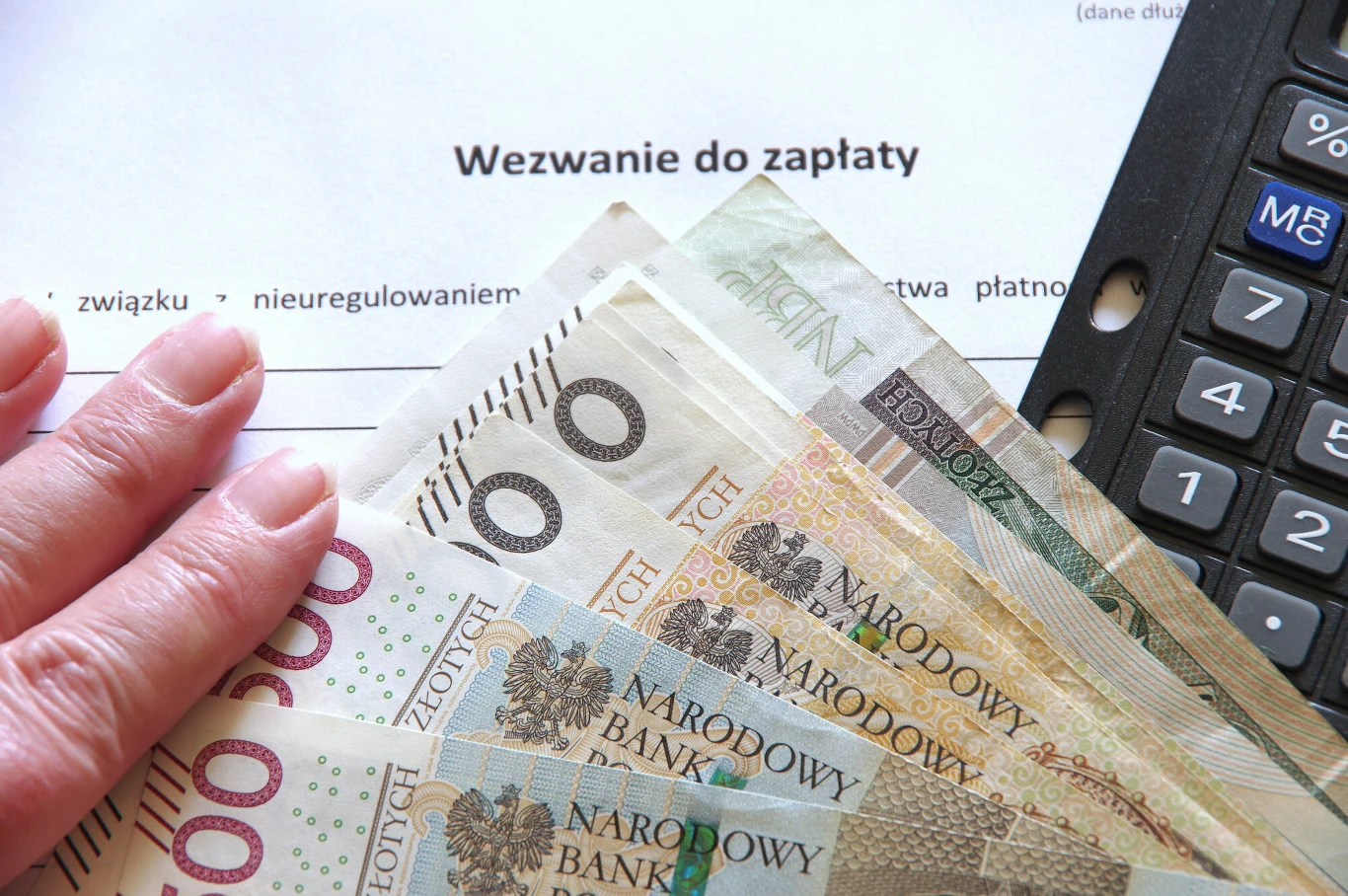 Kiedy komornik może zająć konto dłużnika? Dokument z wezwaniem do zapłaty. Obok pieniądze na stole wraz z kalkulatorem.