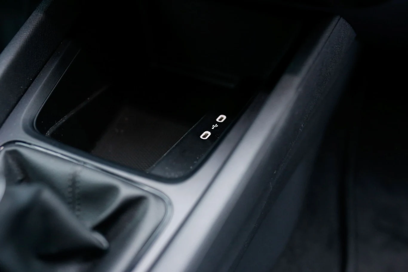 Konsola środkowa samochodu z widocznym portem USB oraz schowkiem obok dźwigni zmiany biegów pokrytej czarną skórą.
