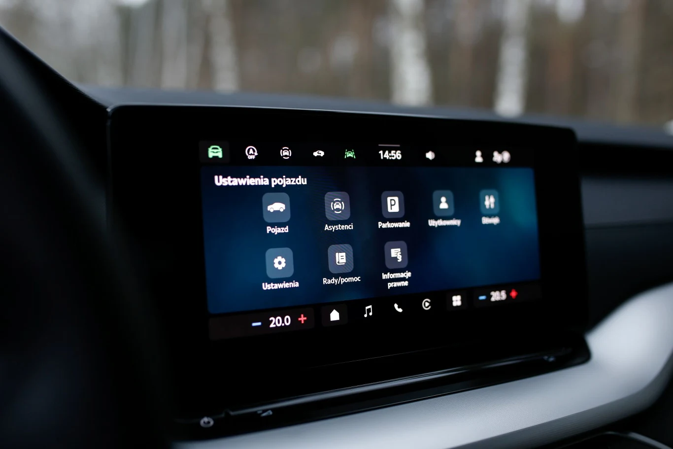 Dotykowy ekran systemu multimedialnego samochodu z wyświetlonym menu ustawień pojazdu, ikonami funkcji takich jak asystent kierowcy, parkowanie, infotainment oraz informacjami o temperaturze i godzinie u dołu ekranu.