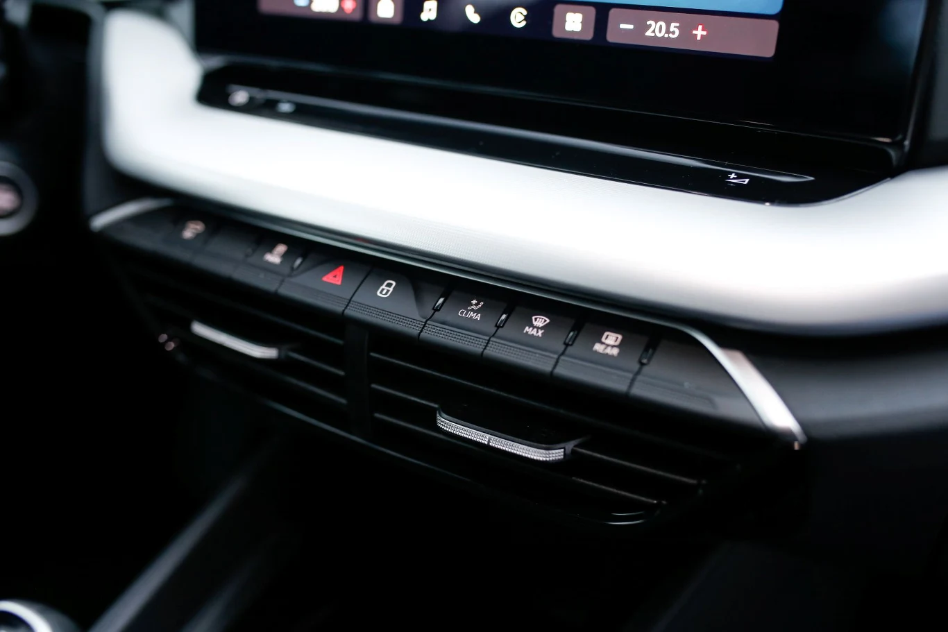 Panel sterowania klimatyzacją w samochodzie z przyciskami do sterowania nawiewem, blokadą drzwi, ogrzewaniem szyb oraz awaryjnymi światłami, położony poniżej dotykowego ekranu multimedialnego.