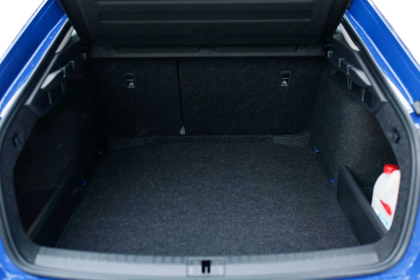 Pojemny bagażnik samochodu z ciemnym wykończeniem tapicerki, po prawej stronie ustawiony biały pojemnik z czerwoną nakrętką.