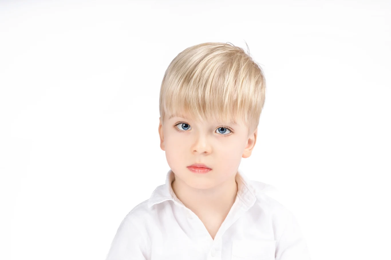 Chłopiec o blond włosach i niebieskich oczach, ubrany w białą koszulę, patrzy poważnie przed siebie na jasnym tle.