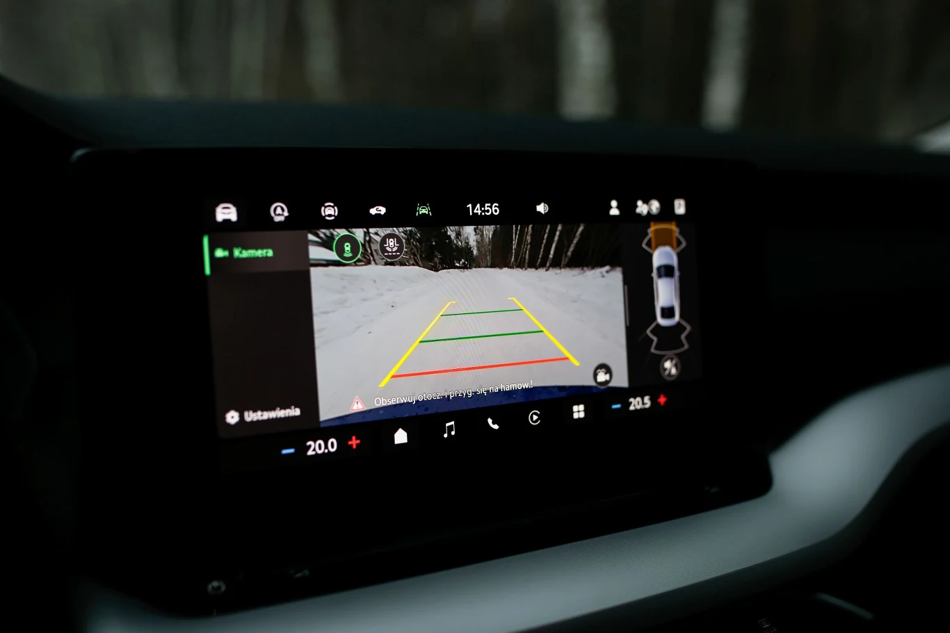 Ekran systemu cofania samochodu z widokiem na ośnieżoną drogę oraz liniami pomocniczymi ułatwiającymi manewrowanie.