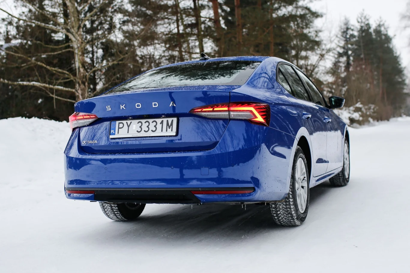 Niebieska Skoda zaparkowana na ośnieżonej drodze, z wyraźnie widocznymi nowoczesnymi tylnymi lampami LED i polską rejestracją otoczona drzewami w zimowym krajobrazie.