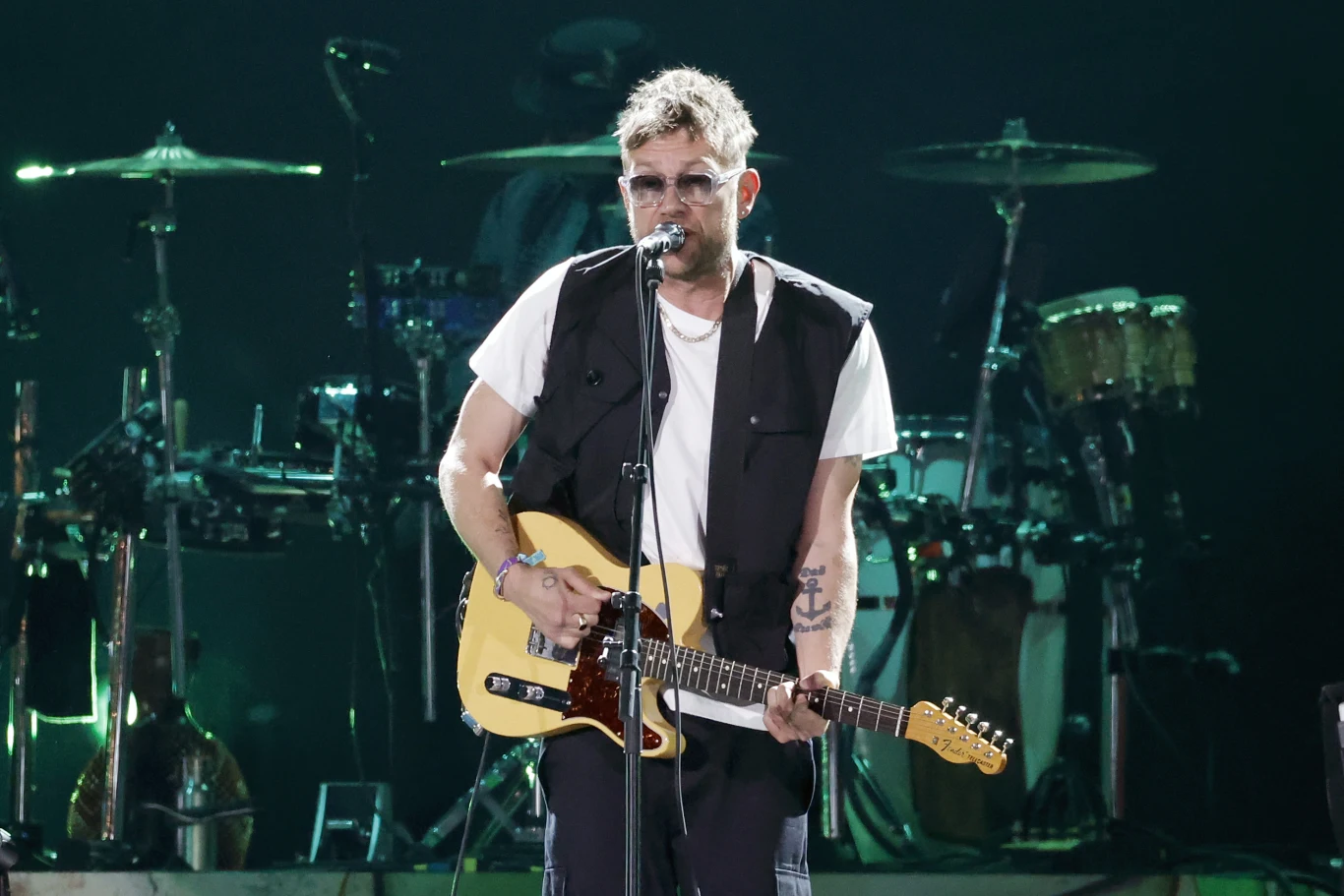 Damon Albarn Damon Albarn śpiewa do mikrofonu i gra na żółtej gitarze elektrycznej na scenie koncertowej.