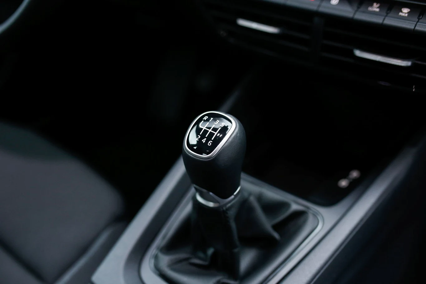 Dźwignia manualnej skrzyni biegów z wyraźnie widocznym schematem przełożeń, otoczona czarną tapicerką i elementami konsoli środkowej samochodu.