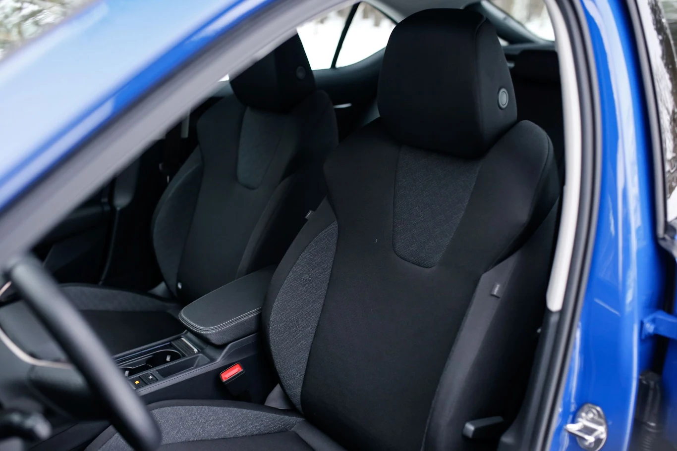 Wnętrze samochodu z widocznymi przednimi siedzeniami w kolorze czarnym, po stronie kierowcy oraz pasażera, nowoczesna konsola środkowa i niebieski lakier na drzwiach.