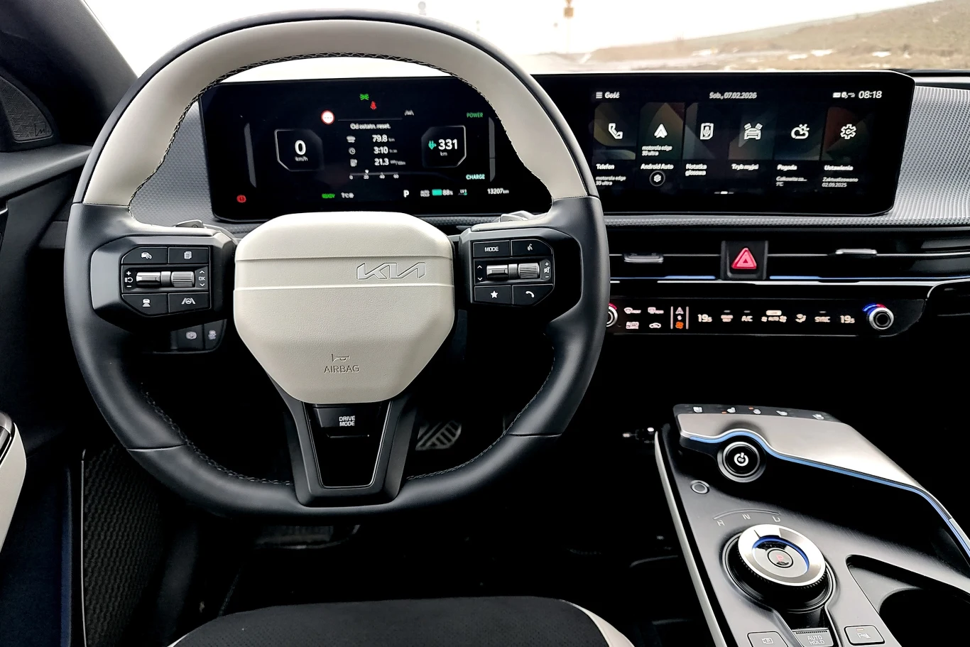 Nowoczesna kierownica z wieloma przyciskami sterującymi, cyfrowy panel wskaźników oraz szeroki ekran dotykowy systemu multimedialnego i zaawansowany panel sterowania konsoli centralnej z selektorem trybów jazdy.