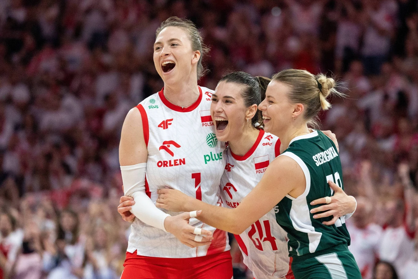 Aleksandra Gryka z dwiema siatkarkami w biało-czerwonych i zielonym stroju podczas meczu, w tle publiczność.