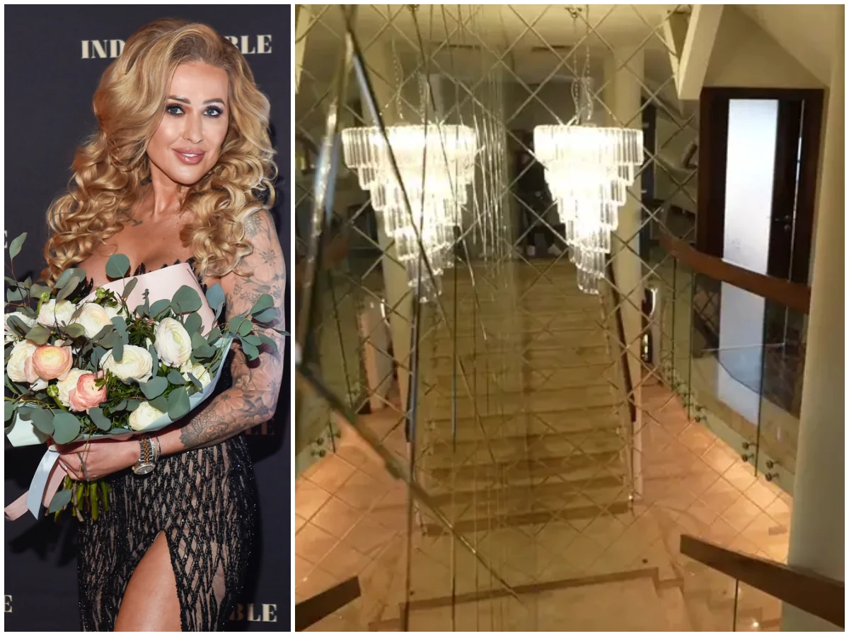 Kobieta o długich, blond włosach w eleganckiej, ciemnej sukni z bukietem białych i różowych kwiatów w rękach obok przestronnego wnętrza z szerokimi schodami, stylowymi żyrandolami i lustrzaną ścianą odbijającą światło.