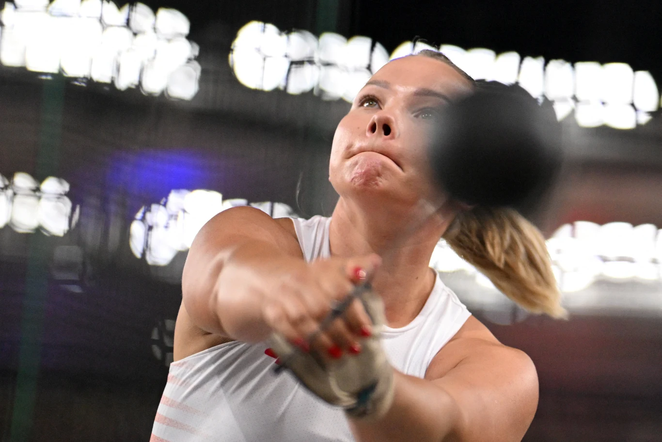 Kobieta koncentrująca się podczas wykonywania rzutu młotem, napięte mięśnie ramion i intensywny wyraz twarzy świadczą o wysiłku włożonym w ruch, tło rozmyte przez dynamiczne obroty młota.