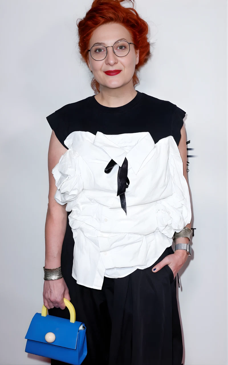 Małgosia Turzańska w biało-czarnej, oryginalnie marszczonej kreacji z czarną kokardą, trzyma w ręku niebieską torebkę z żółtą rączką; jej stylizacja uzupełniona jest srebrnymi bransoletkami i zegarkiem.