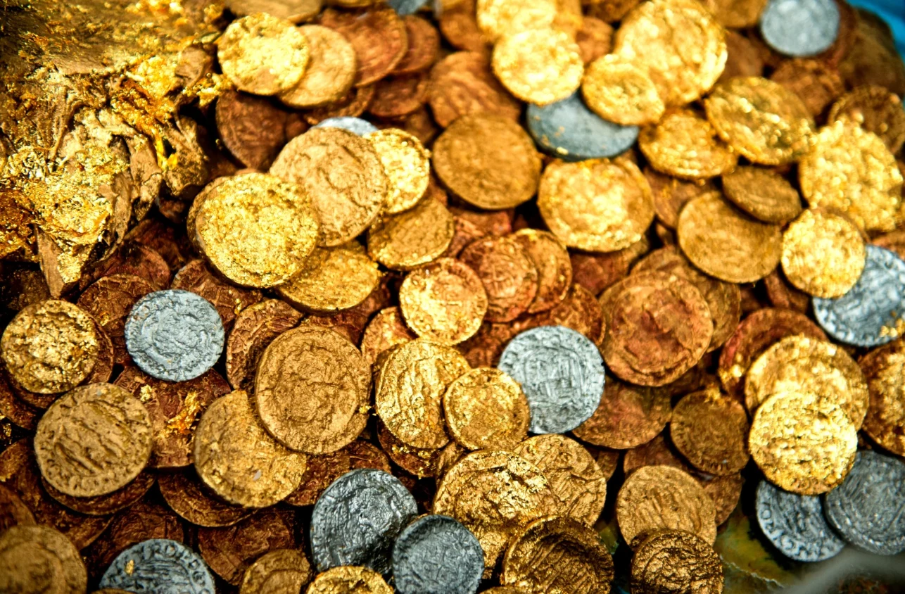 Monety składano w darze - wśród odkryć znajduje się rzadka złota moneta Tetrykusa I. Grafika poglądowa. Stos złotych i srebrnych monet, w tym rzadka złota moneta Tetrykusa I, poglądowa grafika znaleziska.