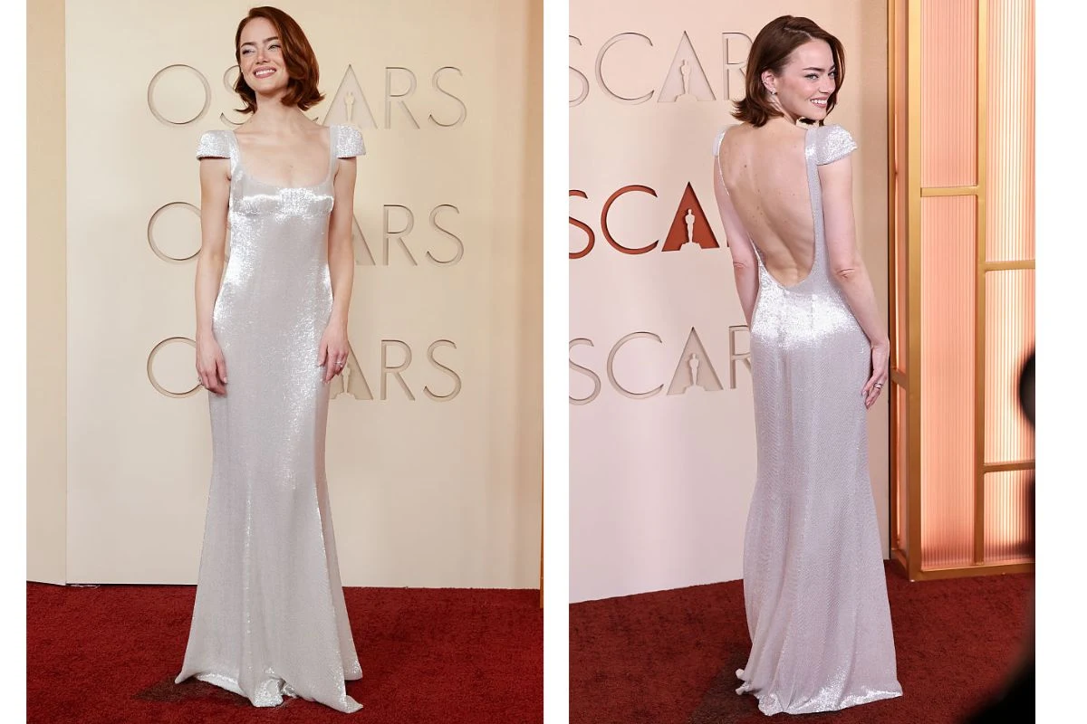 Kobieta w długiej, połyskującej, srebrnej sukni z odkrytymi plecami i krótkimi rękawkami pozuje na czerwonym dywanie przed ścianką z napisem OSCARS.