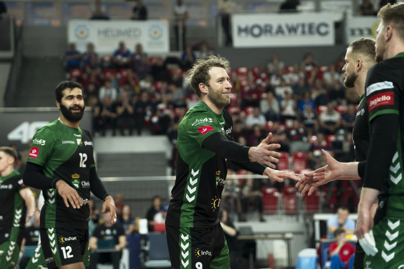 Zawodnicy drużyny siatkarskiej w zielono-czarnych strojach gratulują sobie podczas meczu na hali pełnej kibiców, skupiając się na geście przybicia piątki oraz sportowej atmosferze rywalizacji.