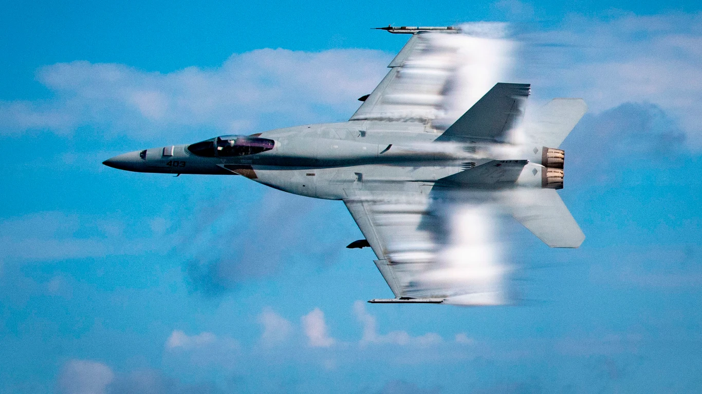 Amerykański myśliwiec przeleciał nisko nad irańskim miastem i otworzył ogień Myśliwiec F/A-18 Super Hornet w locie z dużą prędkością; na skrzydłach widoczne smugi kondensacyjne; w tle błękitne niebo