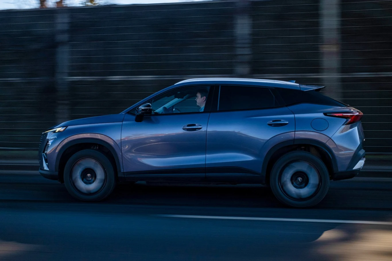 nowoczesny, szary SUV poruszający się po miejskiej drodze, w pojeździe obecny kierowca, w tle betonowa ściana dźwiękochłonna