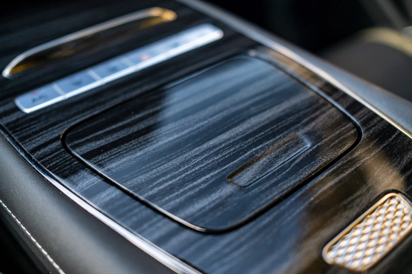 Konsola środkowa samochodu z eleganckim wykończeniem w kolorze czarnego drewna, dotykowymi przyciskami i srebrnymi detalami.