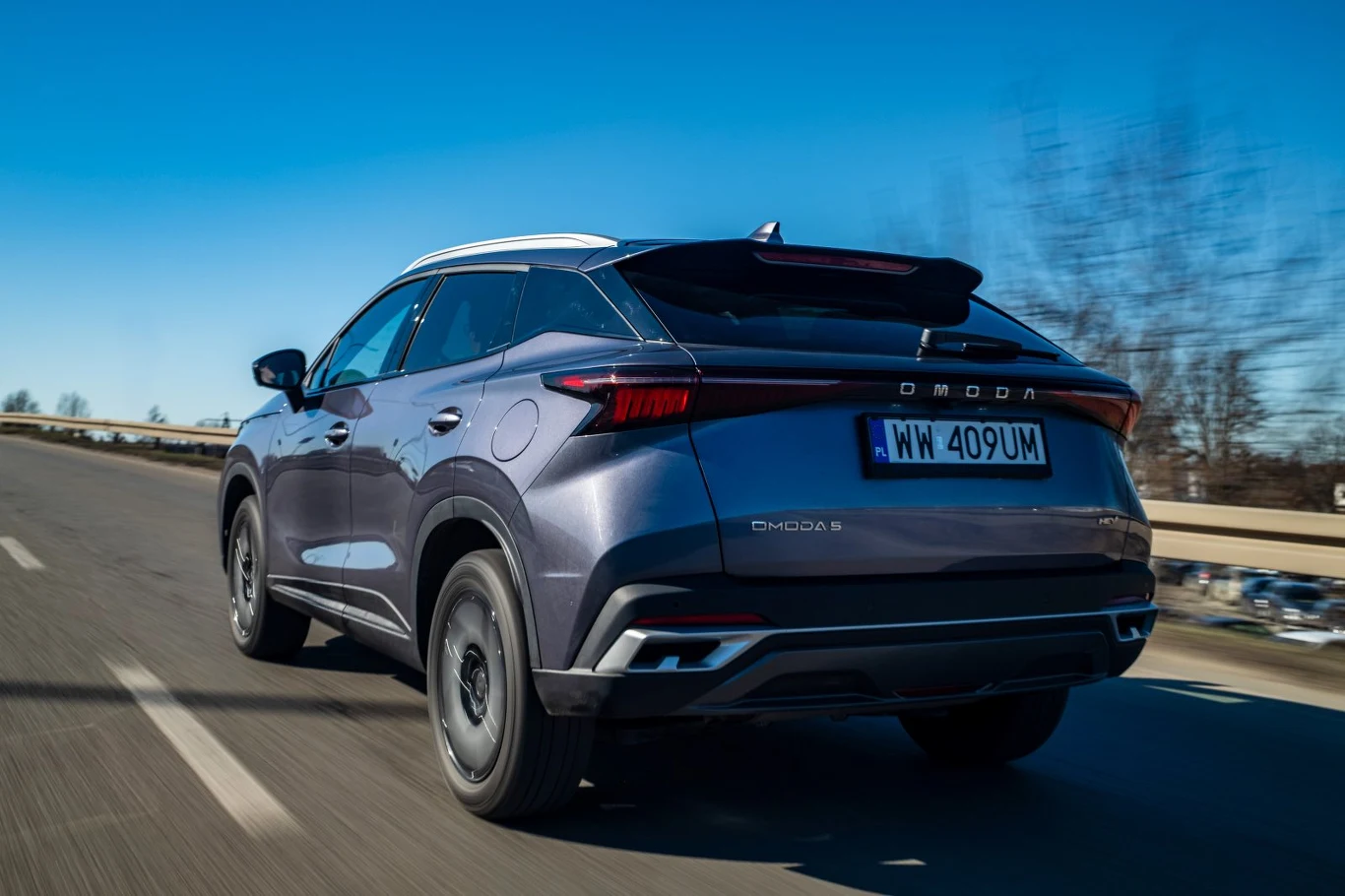 szary nowoczesny SUV marki Dongfeng jedzie po asfaltowej drodze, dynamiczny układ świateł tylnych, wyraźnie widoczna rejestracja oraz opływowe linie nadwozia podkreślające sportowy charakter auta