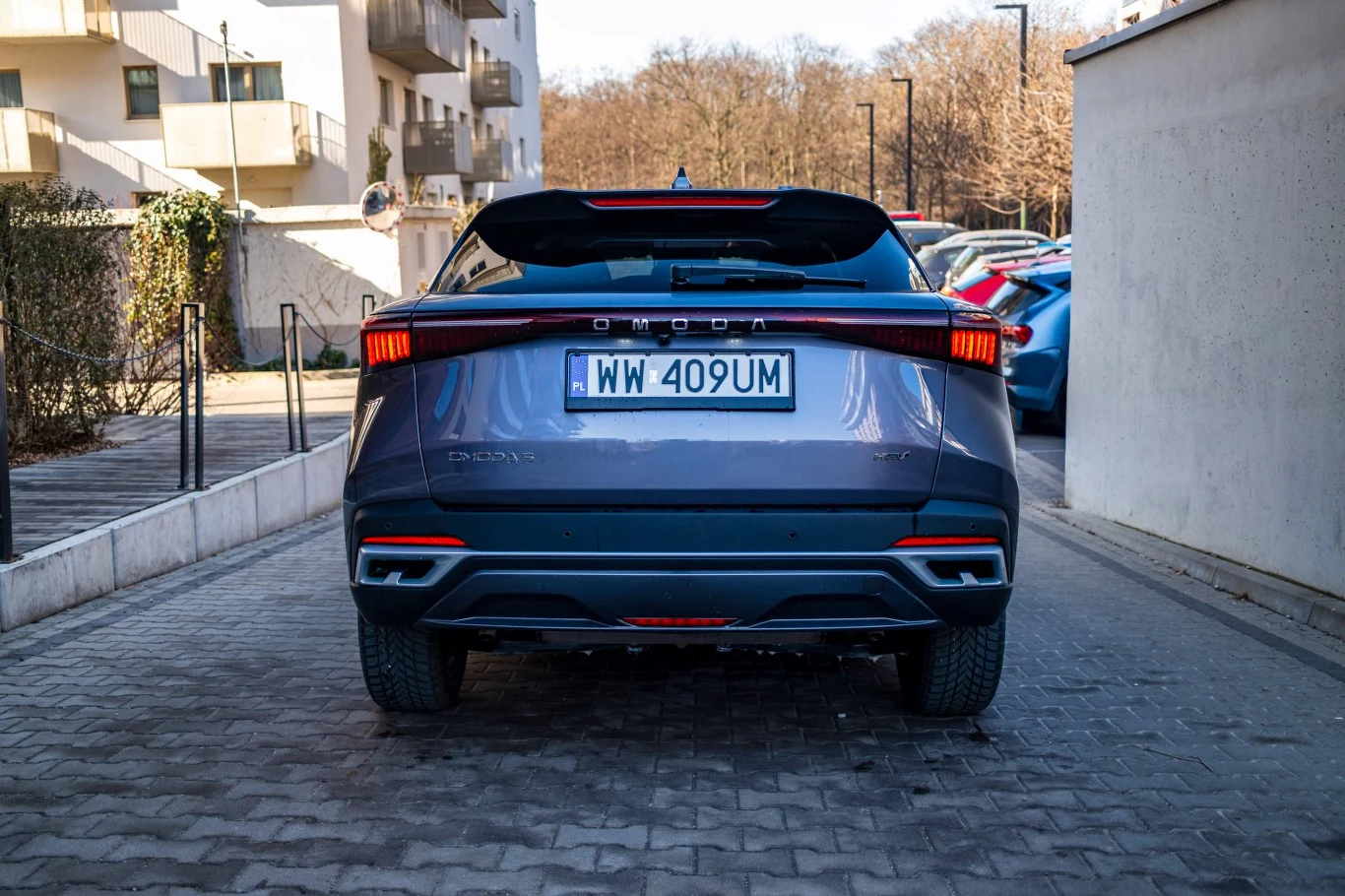 nowoczesny samochód elektryczny marki Skoda o szarym kolorze nadwozia ustawiony tyłem na brukowanej drodze, z charakterystycznymi wąskimi światłami tylnymi i czarnym dachem