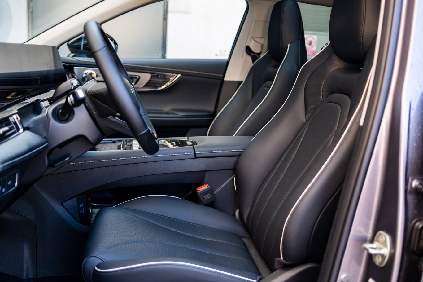 wnętrze nowoczesnego samochodu z czarnymi, skórzanymi fotelami ozdobionymi białymi przeszyciami, elegancką deską rozdzielczą oraz wielofunkcyjną kierownicą